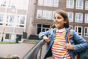 Ein junges Mädchen fröhlich vor der Schule.